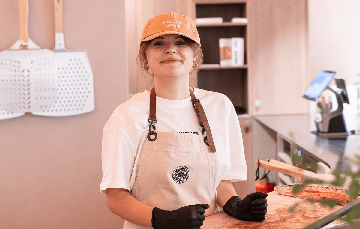 Mitarbeiterin mit Amore Loui Cap und Schürze hinter der Theke
